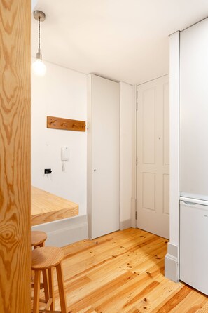 Cozinha compacta com mesa de madeira e banquetas, luminária pendente e geladeira branca.