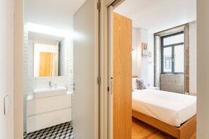 Ein modernes Schlafzimmer mit einem h ölzernen Bett, einem weißen Nachttisch und einem Badezimmer mit Waschbecken und Spiegel.