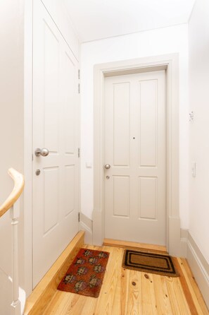 Um corredor com portas brancas, piso de madeira e tapete de entrada.