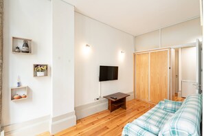 Ein modernes Schlafzimmer mit Fernseher, Holzboden, einem Bett mit Karo-Bettwäsche und einem Schrank mit Spiegel.