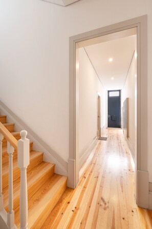 Un intérieur moderne avec un escalier en bois, un couloir menant à une porte sombre et un plancher de couleur claire.