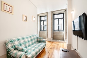 Ein Wohnzimmer mit einem Karo-Sofa, einem Flachbildfernseher und einem Fenster mit Blick auf Gebäude.