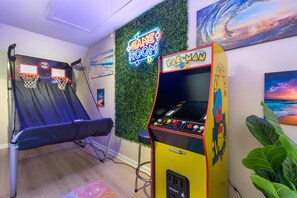 Ein Zimmer mit Trampolin, einer Neonreklame, einer Pac-Man-Spielmaschine und einem Gemälde einer Welle.