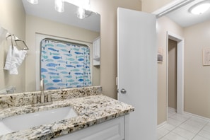 A bathroom with a white sink, marble countertop, and a shower curtain with fish patterns. - Hillside by the Sea - 5BR, sleeps 14, game room (North Myrtle Beach)