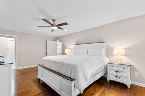 A bedroom with a bed, nightstands, a ceiling fan, and a door leading to another room. - Hillside by the Sea - 5BR, sleeps 14, game room (North Myrtle Beach)