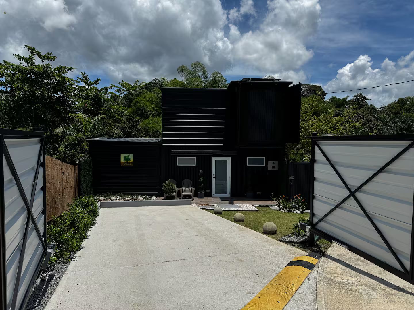 Un bâtiment moderne à deux étages, avec une allée en béton menant à une entrée fermée par un portail.