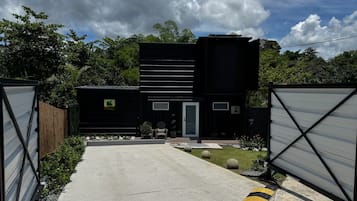 Un bâtiment moderne à deux étages, avec une allée en béton menant à une entrée fermée par un portail.