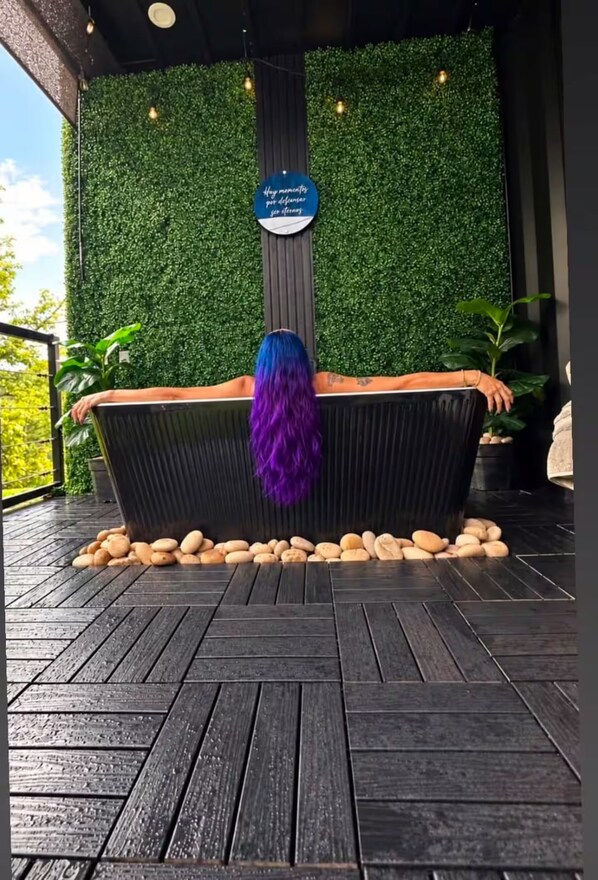 A spa area with a black bathtub surrounded by pebbles, a green wall with a sign, and a wooden deck.