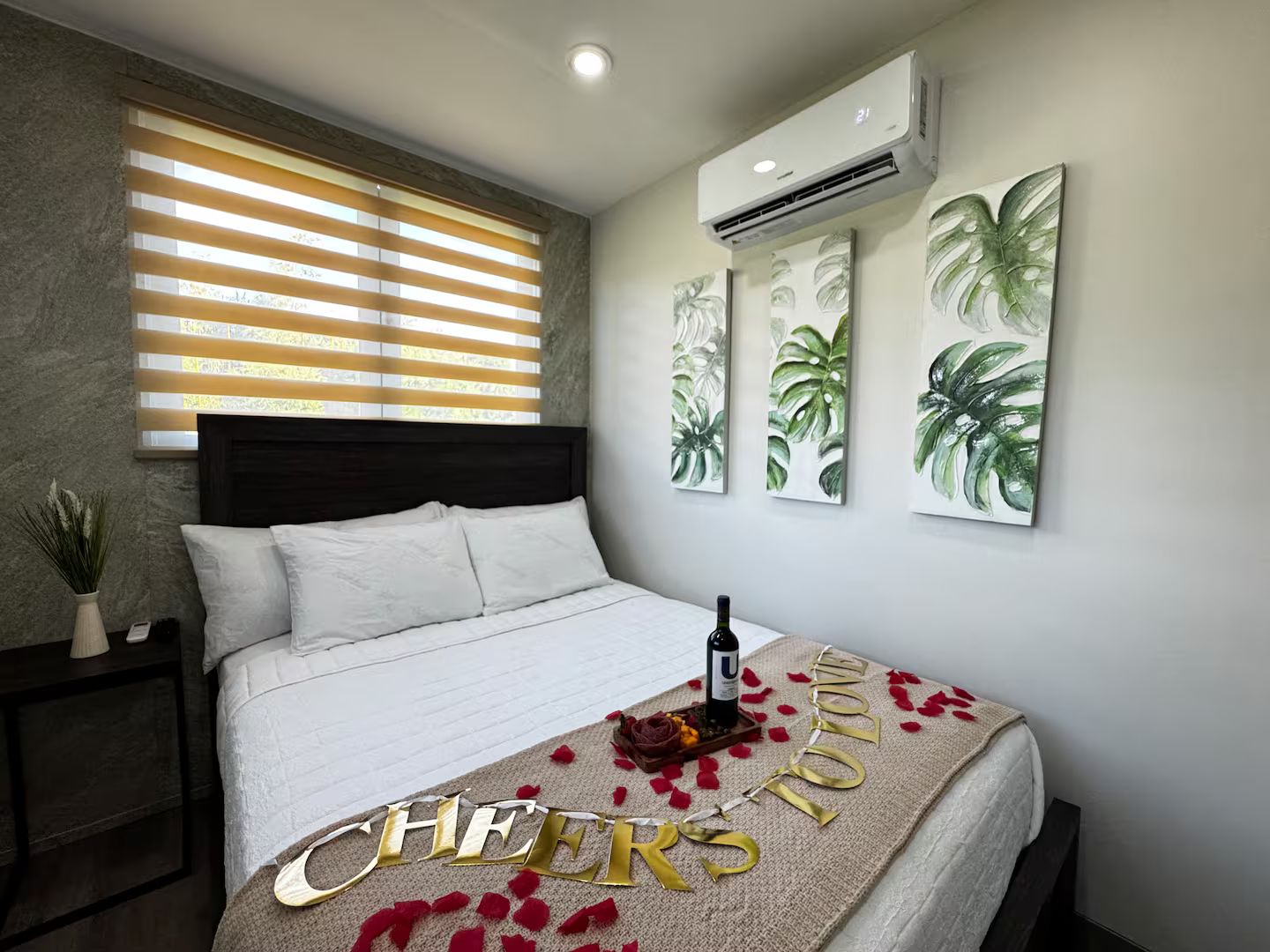 Ein Schlafzimmer mit Bett, einem Fenster mit Jalousien, einer Klimaanlage und Wandbildern.