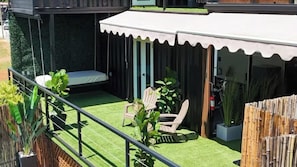 A patio with a swing, two chairs, a small table, and a covered seating area.