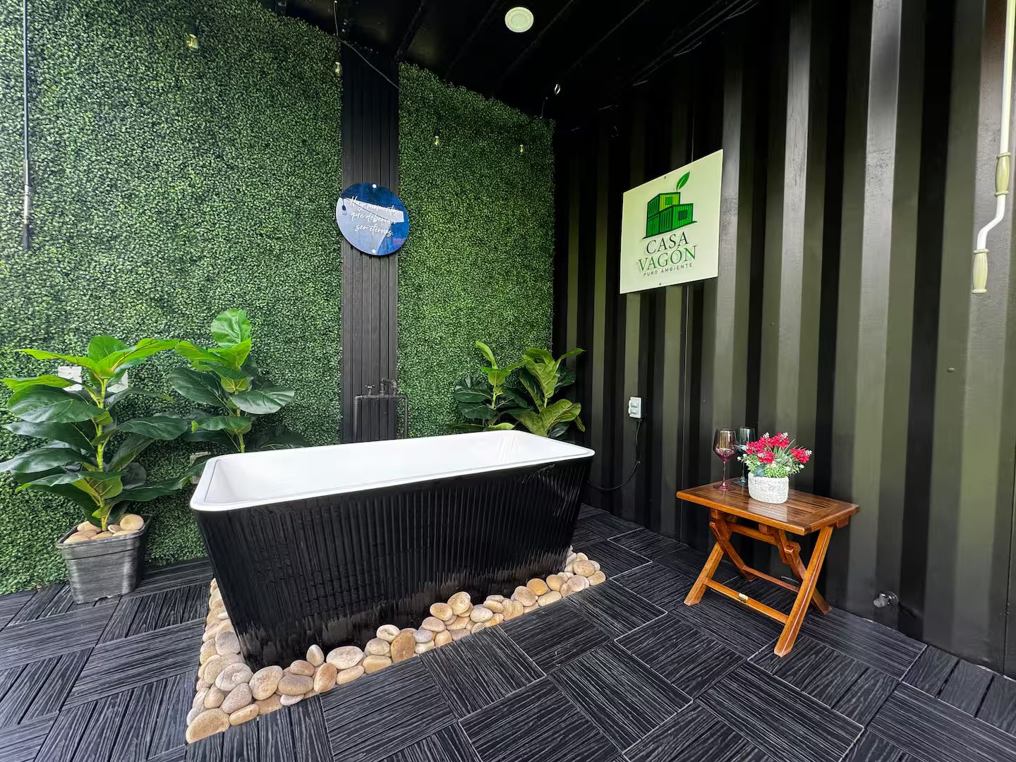 Une salle de bain moderne avec une baignoire noire, un tabouret en bois et une plante en pot.