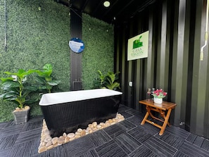 A modern bathroom with a black bathtub, a wooden stool, and a potted plant.
