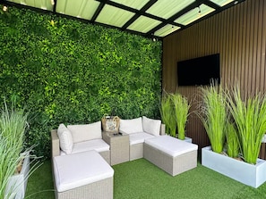 A modern outdoor seating area with a green wall, wicker furniture, and planters.