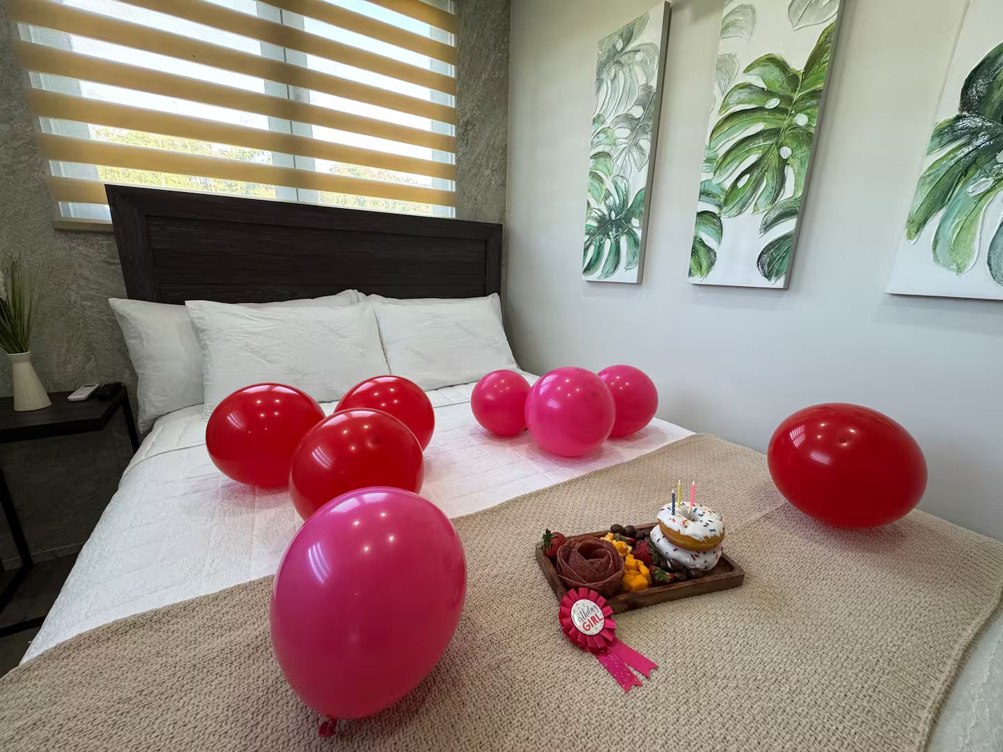 Ein Schlafzimmer mit einem Bett, Luftballons und einem Tablett mit Kuchen und Schleife.
