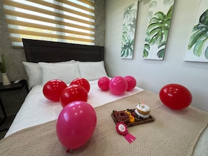 A bedroom with a bed, balloons, and a tray with a cake and a ribbon.