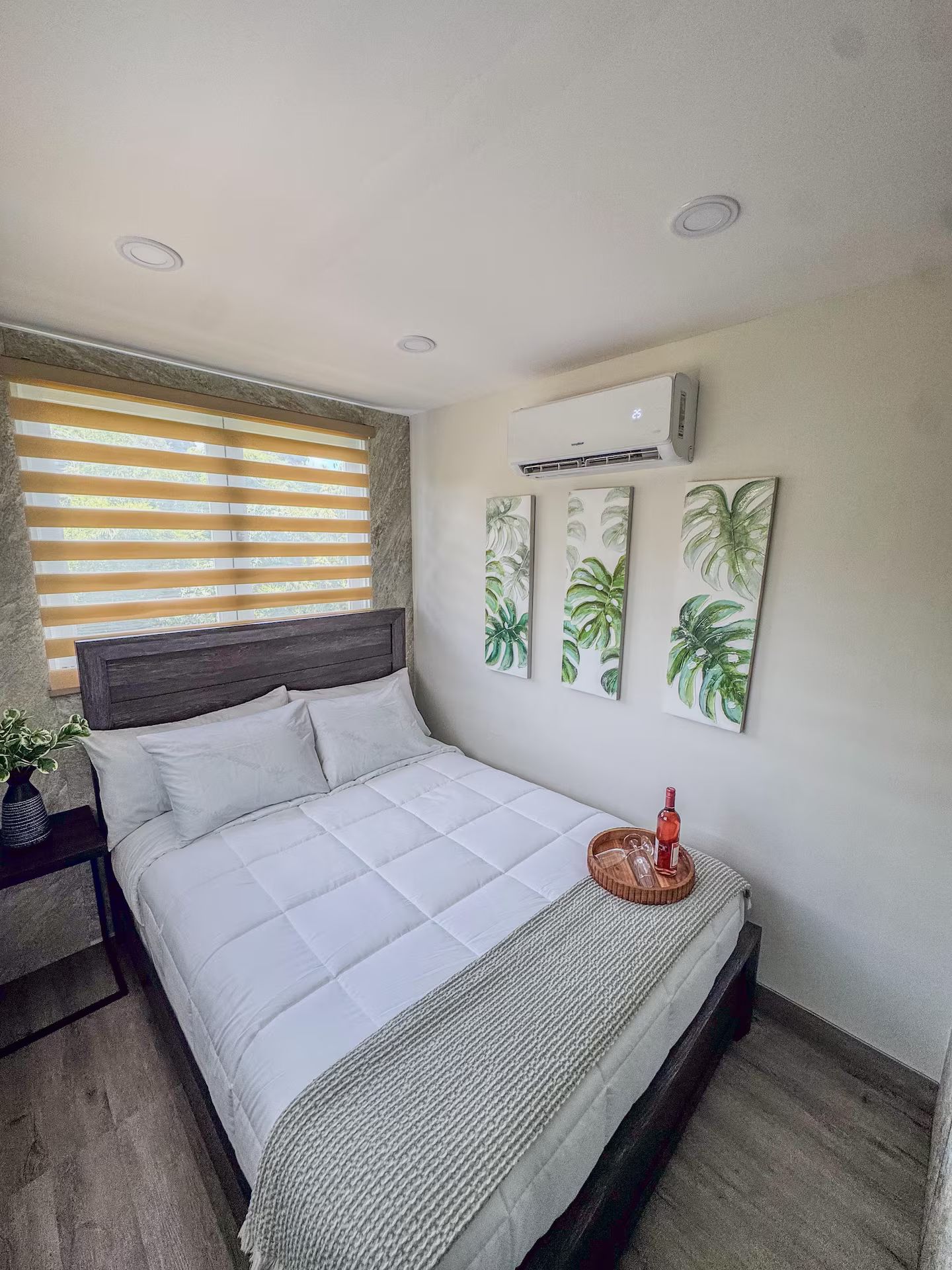 Une chambre à coucher comprenant un lit, une fenêtre avec des stores, un appareil de climatisation et des œuvres d’art murales.