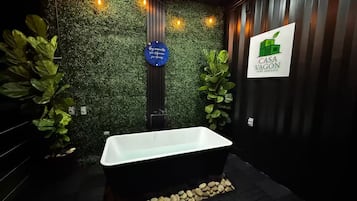 Un baño moderno con una bañera independiente, una pared verde con follaje y un letrero que dice Casa Vagon.