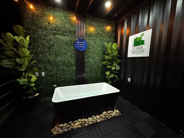 A modern bathroom with a freestanding bathtub, a green wall with foliage, and a sign for Casa Vagon.