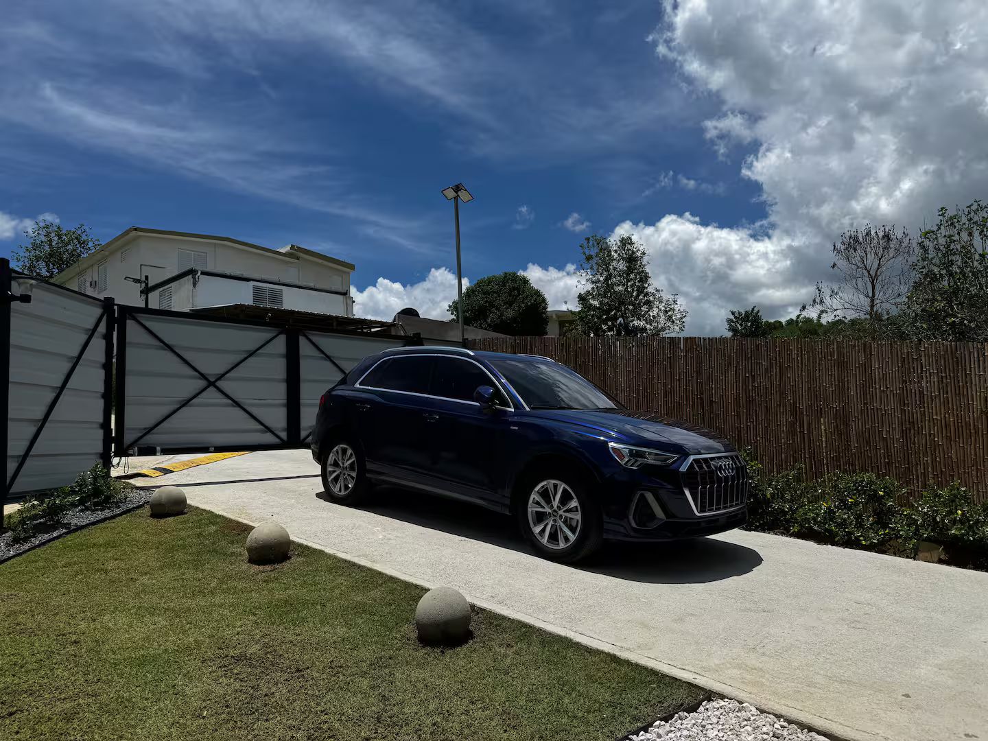 A dark-colored SUV parked in a driveway with a gated garage, a wooden fence, and a clear sky.