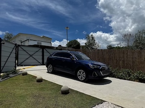 A dark-colored SUV parked in a driveway with a gated garage, a wooden fence, and a clear sky.