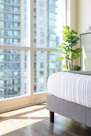 A bedroom with a large window, a bed with a white pillow, and a green plant. - Sleek Studio in Fort York Near Lake & Liberty (Toronto)