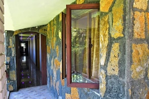 Um corredor de pedra com uma janela emoldurada em madeira e uma porta que dá para outro quarto.