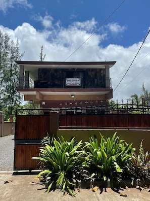 Um edifício de dois andares com varanda, placa de identificação e entrada com portão.