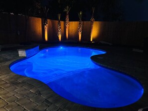 A swimming pool with a curved edge, surrounded by a wooden fence and palm trees. - One-Block Beach Oasis w/ Poolside Game & Golf Cart (Panama City Beach)