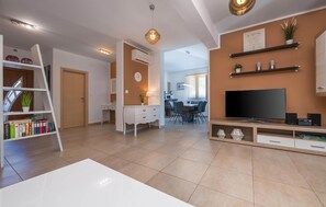 A modern living room with a flat-screen TV, a white desk, a bookshelf, and a dining area. - Lovely home in Kavran with private swimming pool, can be inside or outside (Kavran)