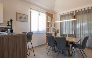Un comedor moderno con una mesa y sillas de madera, una zona de cocina con cafetera y una ventana con vistas.