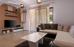 Ein Wohnzimmer mit Flachbildfernseher, Couchtisch, Sofa und einem fenster mit Vorhängen.