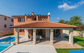 Una casa de dos pisos con un patio cubierto, una piscina y un muro de piedra.