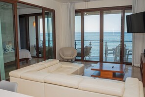 Een ruime woonkamer met een grote bank, een houten salontafel en een balkon met uitzicht op zee.