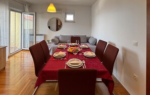 Ein Essbereich mit einem Tisch für vier Personen, einer Couch, einem Spiegel und einem fenster mit Vorhängen.