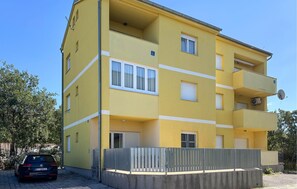 A multi-story yellow building with balconies, a satellite dish, and a car parked in front. - Amazing apartment in Jadranovo with house sea view (Jadranovo)