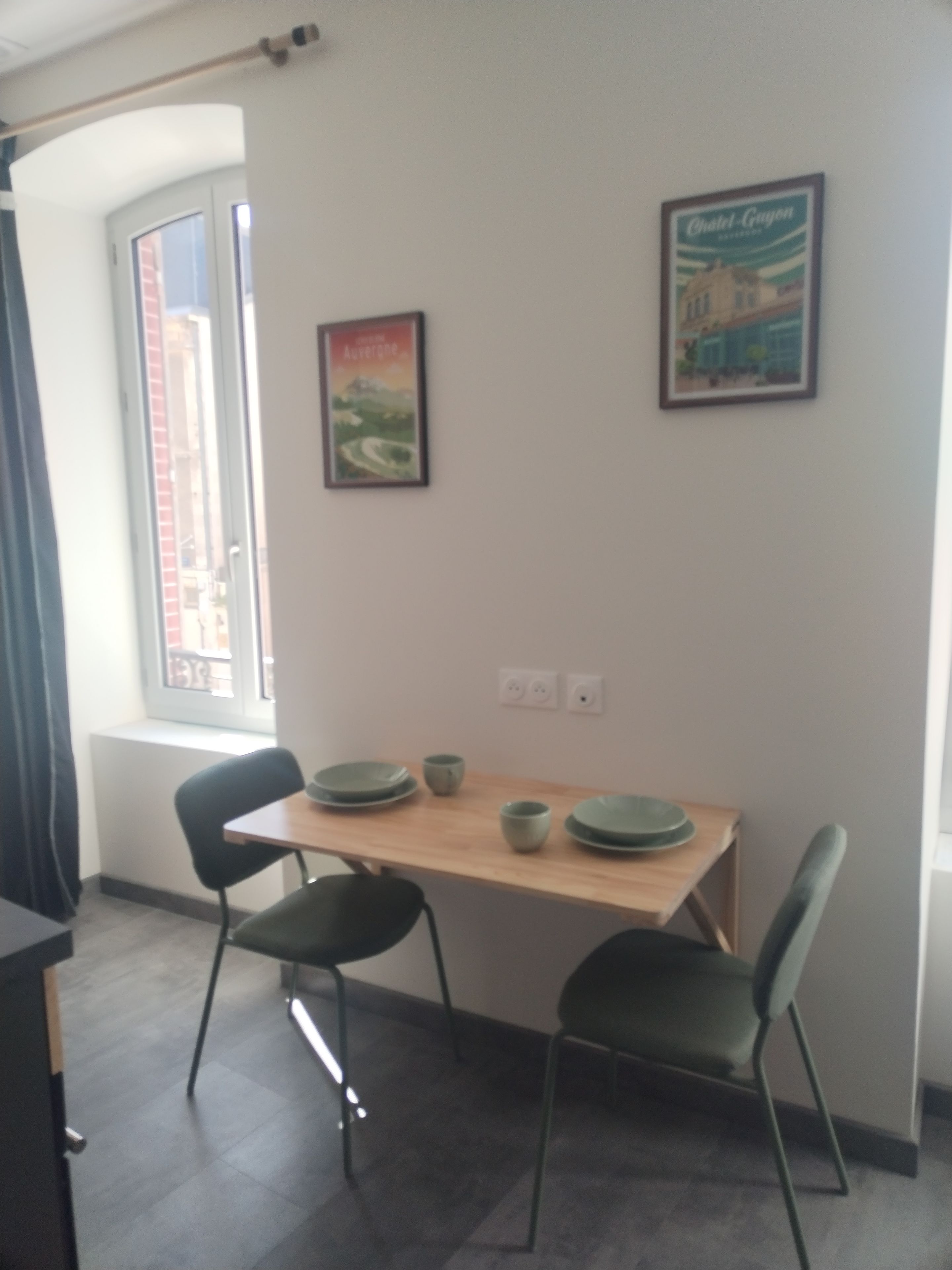 Ein Essbereich mit Tisch, Stühlen und einem Fenster. An der Wand hängen zwei gerahmte Bilder.