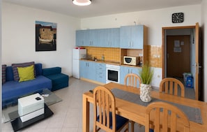 Ein gemütlicher Wohnbereich mit Küchenzeile, einem Essbereich mit Holzsesseln, einem blauen Sofa mit Kissen und einem kleinen Tisch.