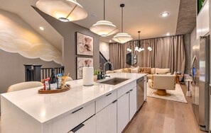 A modern kitchen with a central island, pendant lighting, and a staircase leading to an upper level. - Nash Lux - Pool/Hot tub - 11 beds - Game Room! (Nashville)