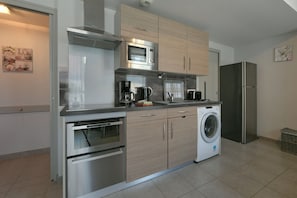 Cozinha moderna com eletrodomésticos de aço inoxidável, armários de madeira e máquina de lavar embutida.