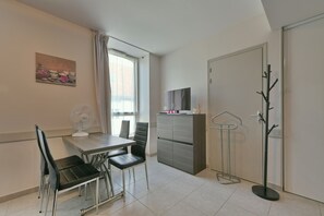 Een compacte, moderne kamer met een eettafel, stoelen, een televisie, een kapstok en een deur.