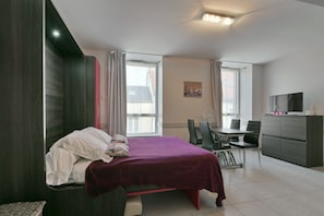 Een moderne slaapkamer met een bed, een bureau, een stoel, een televisie en een raam.