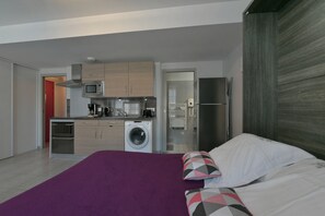 Ein kompaktes Hotelzimmer mit Bett, Waschmaschine, Mikrowelle und einer kleinen Küchenzeile.