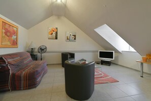 A loft-style living room with a sofa, a black ottoman, a flat-screen TV, and artwork on the walls. - L'Oranger - Petfriendly - Jacuzzi, sauna (La Ferrière-aux-Étangs)