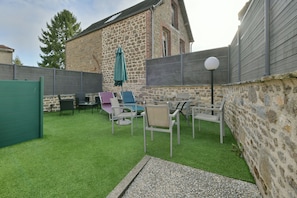 Een terras met kunstgras, tuinmeubilair en een stenen gebouw op de achtergrond.