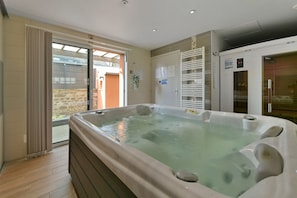 Een wellnessruimte met een bubbelbad, een schuifdeur naar een balkon en een sauna.