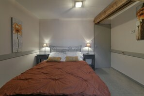 Een slaapkamer met een bed, twee nachtkastjes met lampen, een deur en een muur met een schilderij.