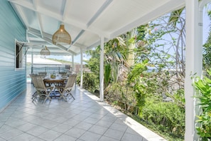 A covered patio with a dining table and chairs, surrounded by lush greenery and a view of the ocean. - Villa Rosalie - Piscine - Proche plage (Le Diamant)