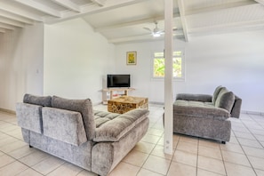 A spacious living area with two grey sofas, a wooden coffee table, a flat-screen TV, and a ceiling fan. - Villa Rosalie - Piscine - Proche plage (Le Diamant)