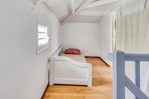 A small, single-bed room with a wooden floor, white walls, and a window with a curtain. - Villa Rosalie - Piscine - Proche plage (Le Diamant)