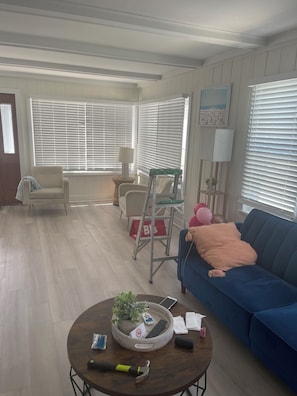 A living room with a blue sofa, a coffee table with a plant, a ladder, and a door with a 'B&B' sign. - Admiral's Suite 300ft to Beach and Boardwalk (Seaside Heights)